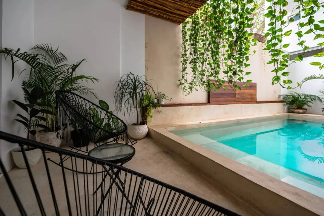 Central40_1-1 (1) Area relax a bordo piscina con due moderne sedie nere e un tavolino, con vista sulla piscina e sulle piante circostanti.